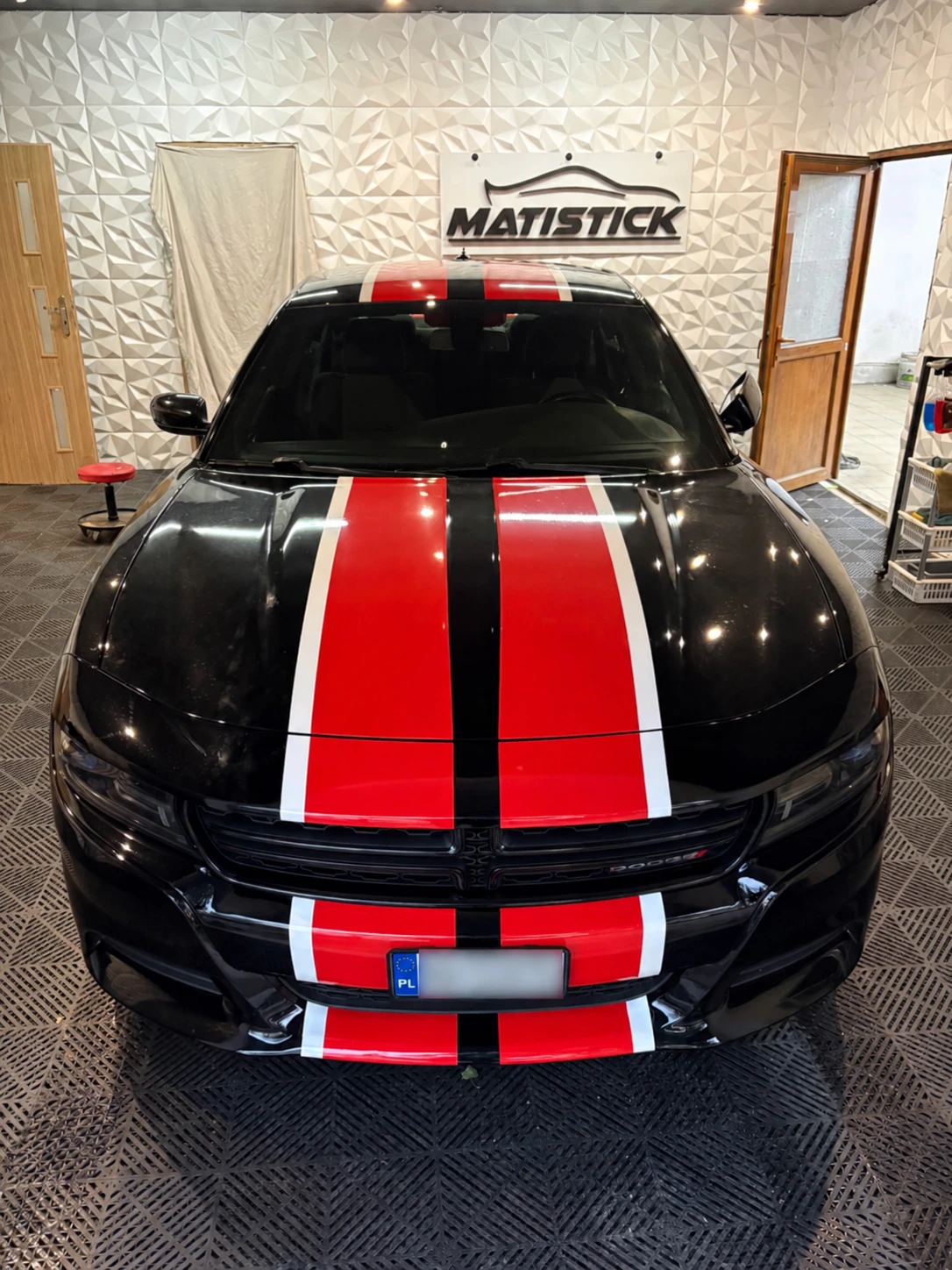 Czarne auto z czerwonymi pasami w warsztacie MATISTICK; tablica zamazana